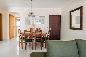 A dining area with a wooden table and chairs, a hanging light fixture, framed artwork on the wall, and a green sofa in the foreground. - Modern & Central 2 bedroom at Rabat Hassan City Center / 3min train station (Rabat)