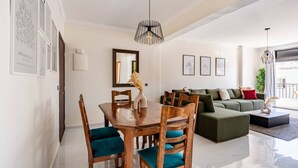Un salon moderne avec un coin repas, comprenant une table à manger en bois, un canapé vert et un grand miroir.