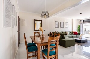 A modern living room with a dining area, featuring a wooden dining table, green sofa, and a large mirror. - Modern & Central 2 bedroom at Rabat Hassan City Center / 3min train station (Rabat)