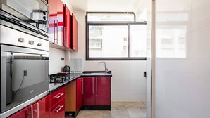 Une cuisine moderne dotée d’appareils électroménagers en acier inoxydable, de meubles de rangement rouges et d’une grande fenêtre laissant entrer la lumière naturelle.