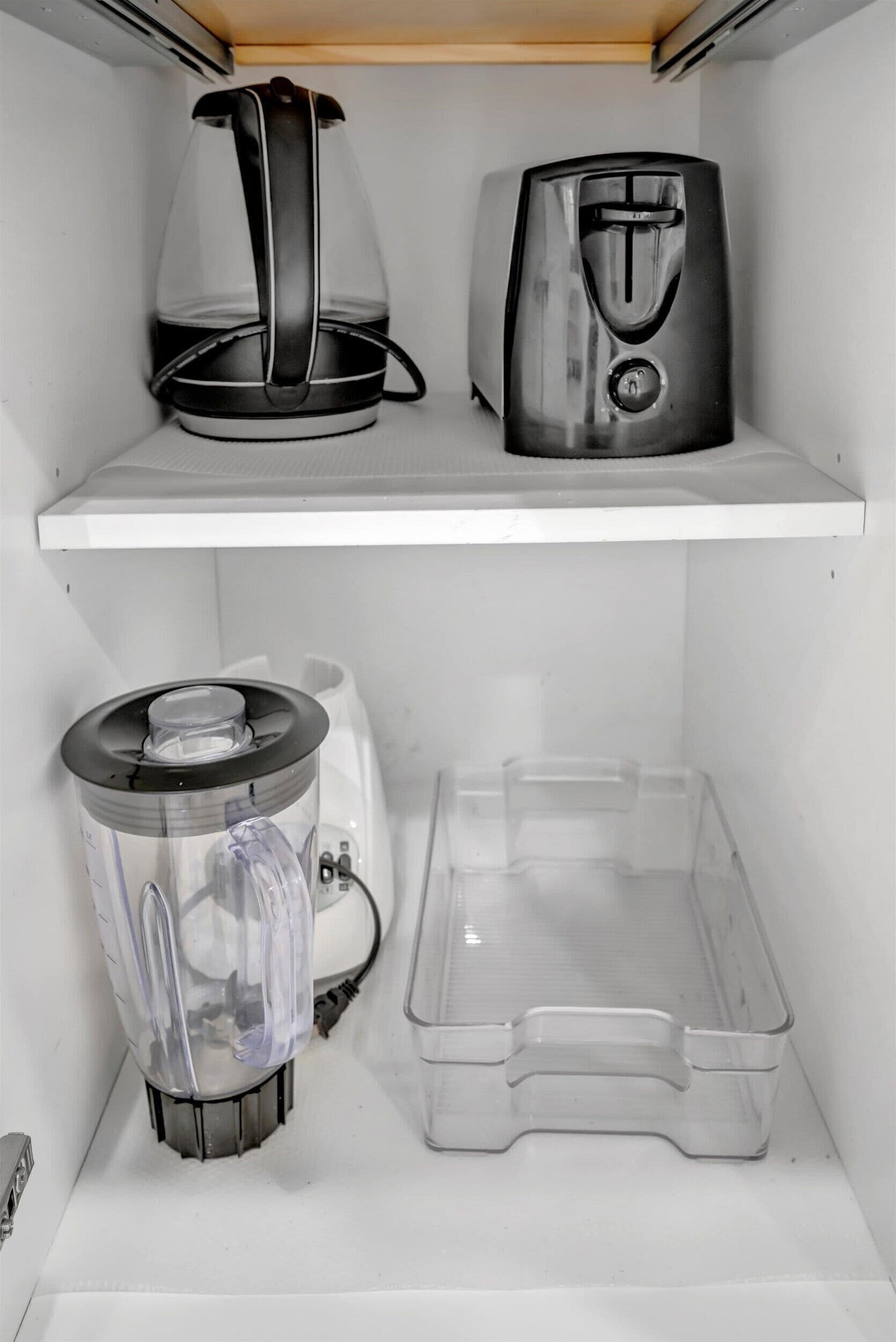 Cozinha com cafeteira, torradeira, liquidificador e um recipiente de plástico transparente sobre o balcão.