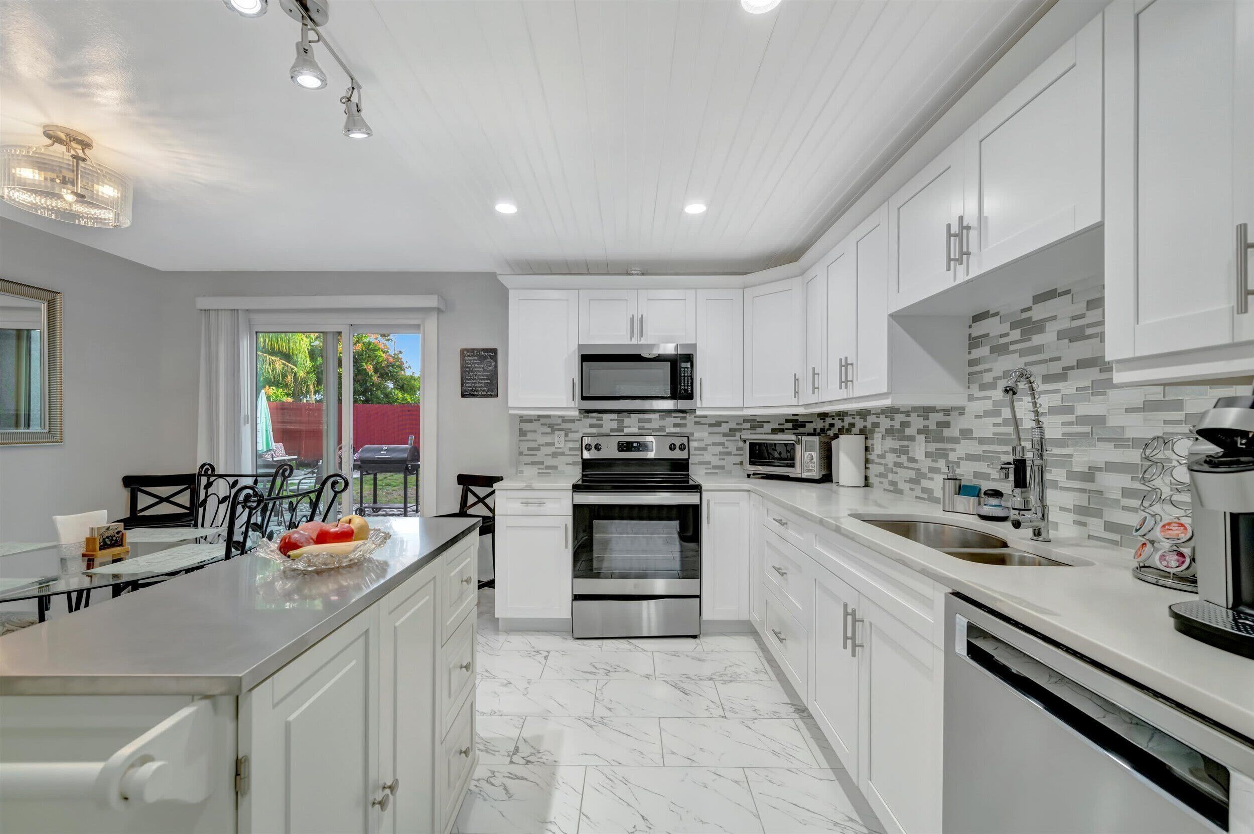Una cocina moderna con armarios blancos, horno de acero inoxidable, microondas y salpicadero de azulejos.