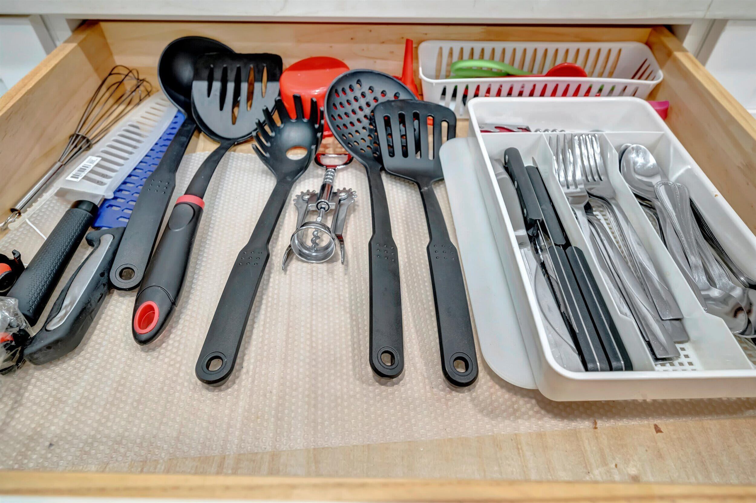 Un cajón con varios utensilios de cocina ordenados, incluyendo espátulas, batidores y un abrelatas.