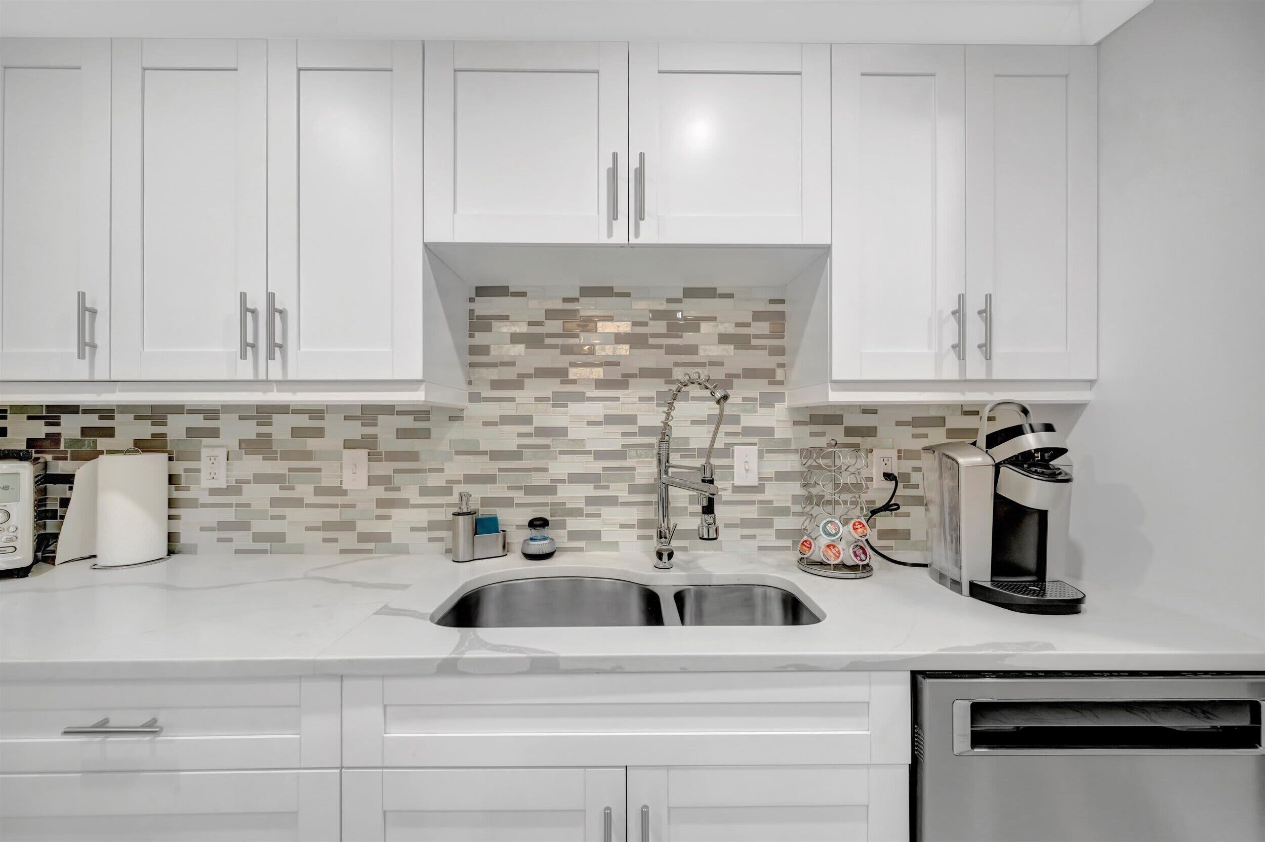 A modern kitchen with white cabinets, a stainless steel sink, and a mosaic backsplash.