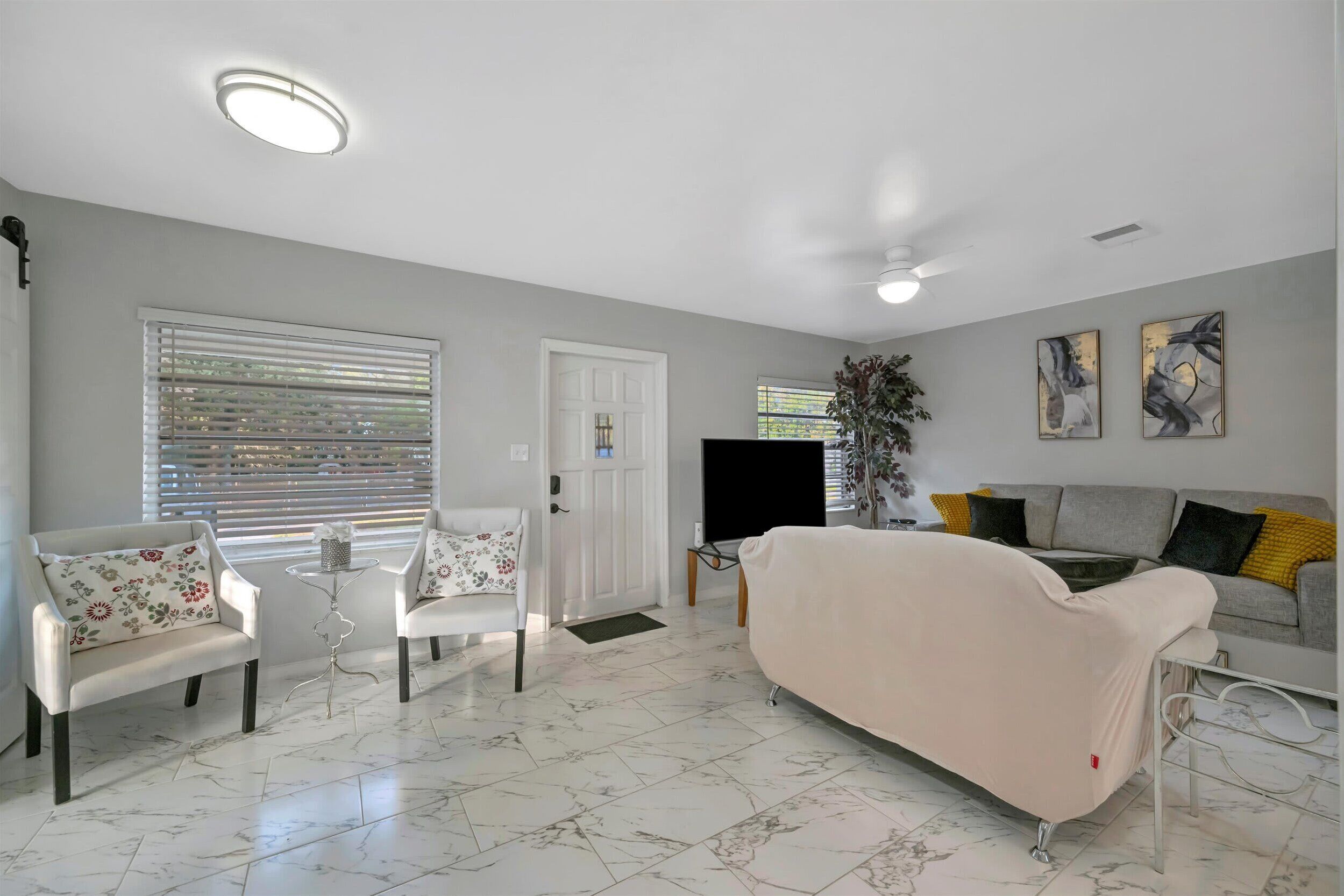 Un salon avec un canapé blanc, deux fauteuils, une table basse et un téléviseur.