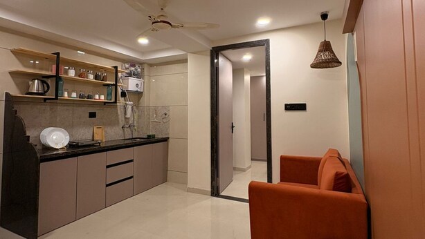 A modern kitchen with a countertop, cabinets, and a ceiling fan. There is a dining area with a sofa and a small ottoman. - Aesthetic 1bhk luxe Indore (Indore)