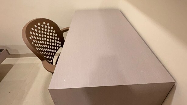 A corner of a room with a white wall, a beige floor, a white table, and a brown perforated chair. - Aesthetic 1bhk luxe Indore (Indore)