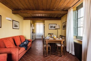 A cozy room with a wooden ceiling, a dining table set with breakfast, a sofa, and a kitchen in the background.