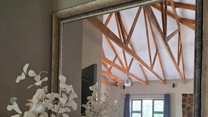 Un salon doté d’un grand miroir qui reflète l’intérieur de la pièce, notamment un plafond avec des poutres en bois, un canapé et une table basse.