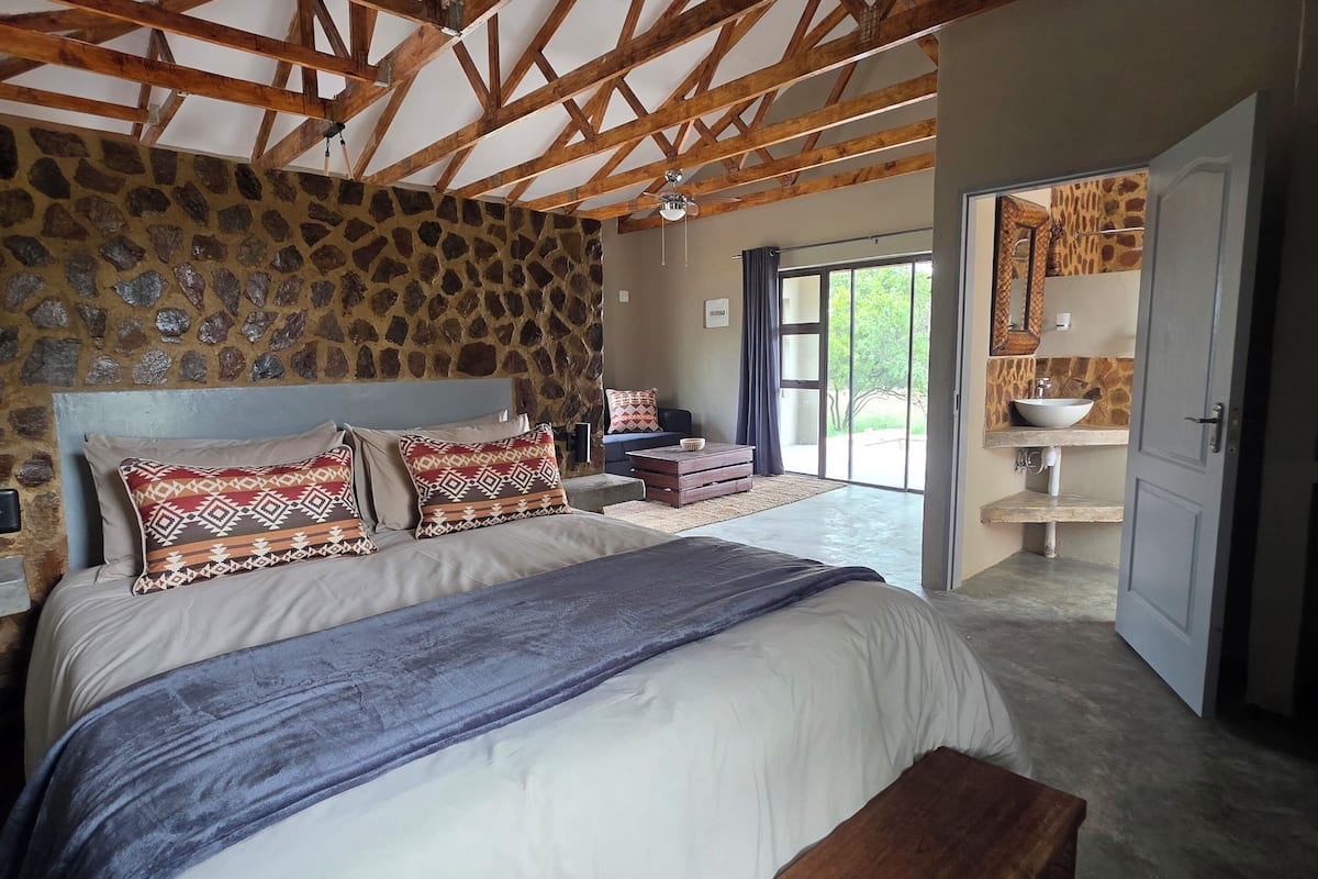 Ein Schlafzimmer mit einem großen Bett, Holzbalken, einer Steinwand und einem Badezimmer mit einem SteinklopfZuber.