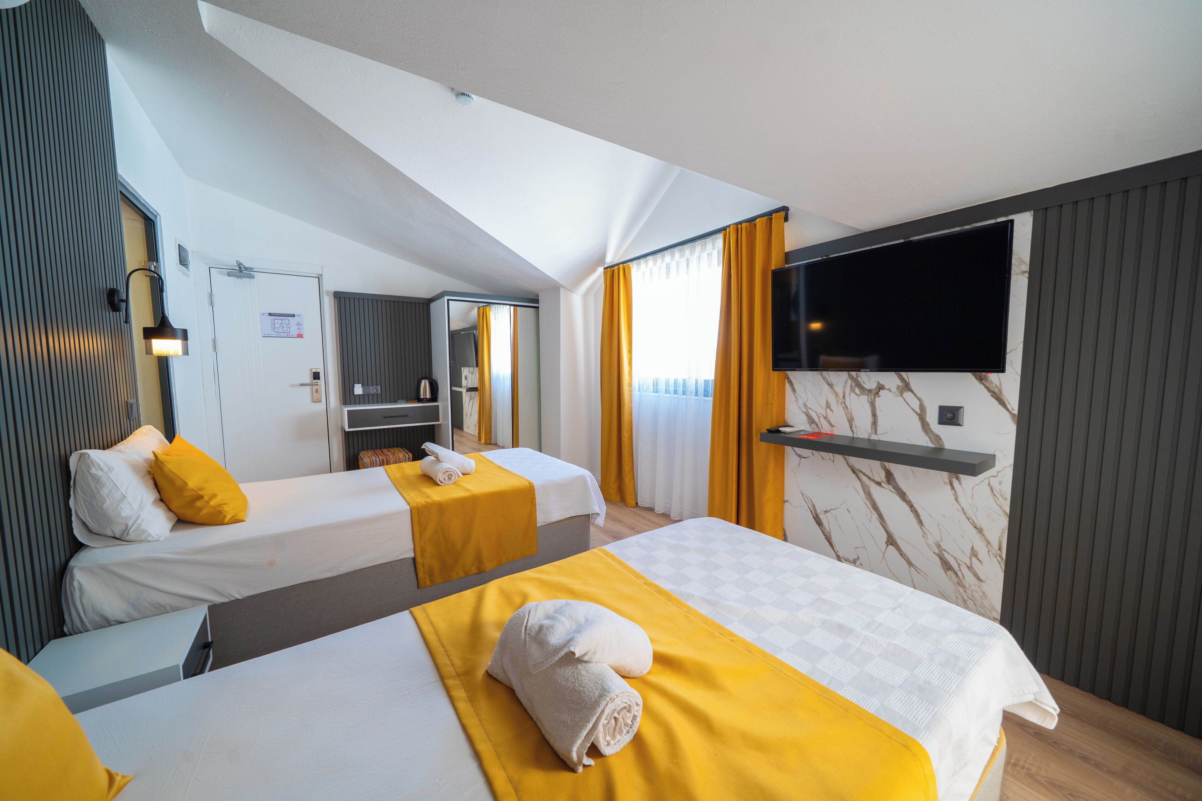 A hotel room with two beds, a TV, a mirror, and a window with curtains.