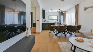 Een moderne keuken met donkere kastjes, een eethoek met een ronde tafel en een woonkamer met een bank en een klok aan de muur.
