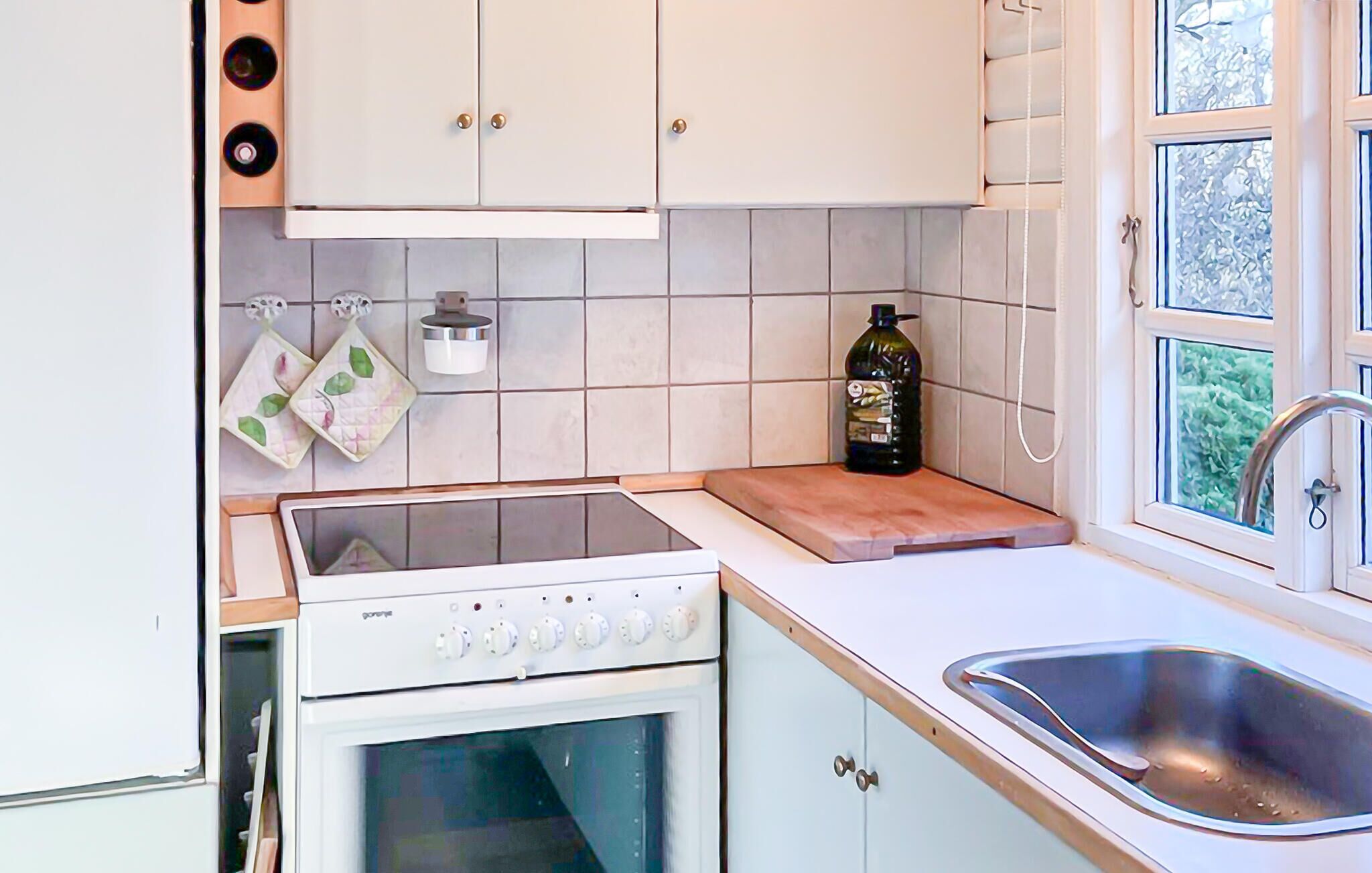 A kitchen with white cabinets, a stove, a sink, and a window with a view of greenery.