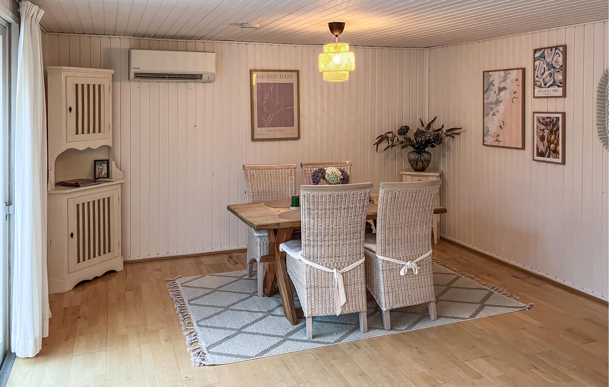 Un coin repas avec une table en bois et des chaises en osier, un luminaire suspendu et des œuvres d’art encadrées accrochées aux murs.