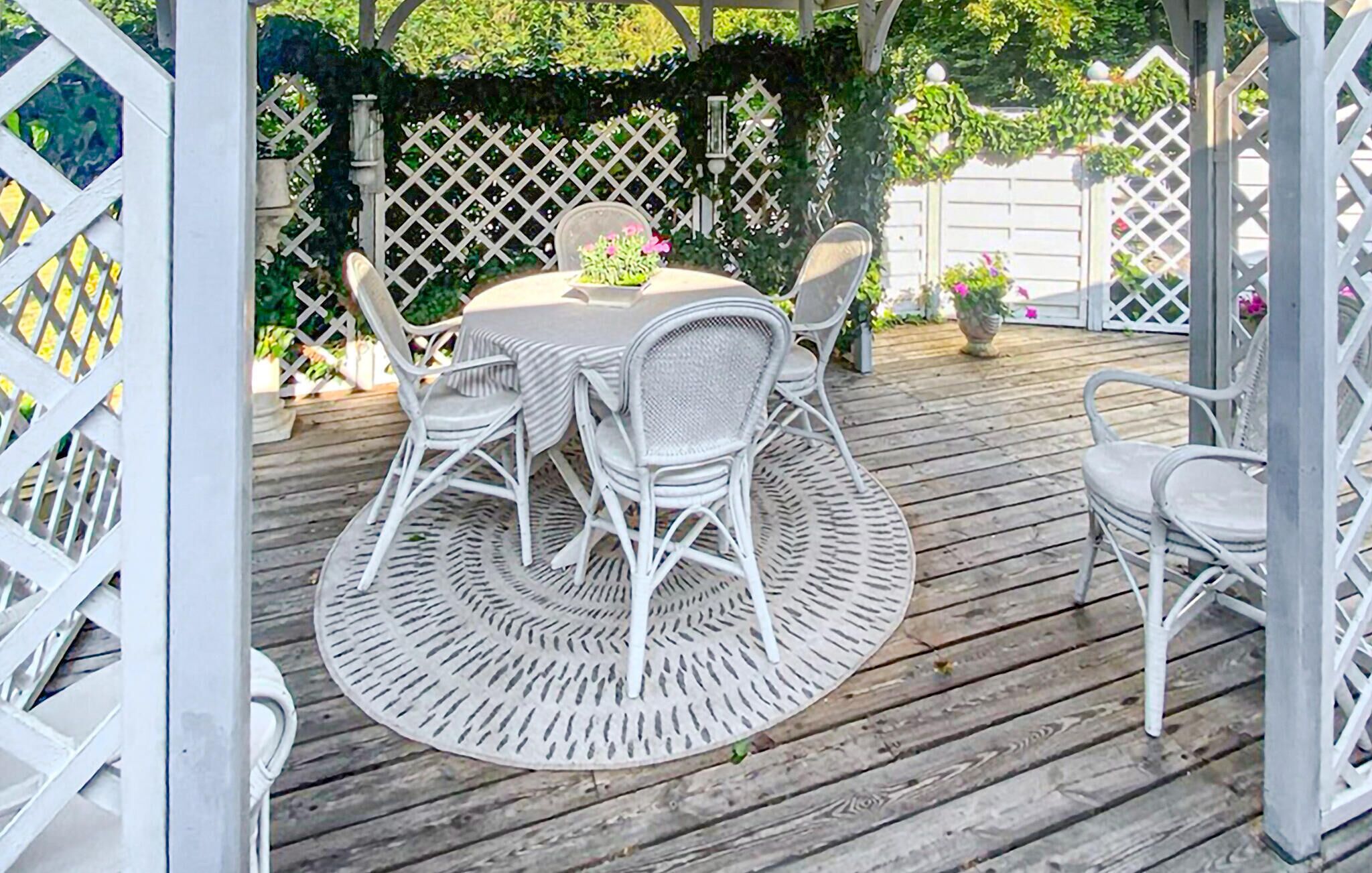 Een overdekte terras met een ronde tafel en witte rieten stoelen.