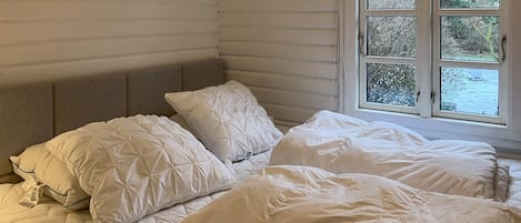 Et soveværelse med seng, puder og et vindue med udsigt til træer.