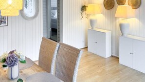 Een kamer met een rieten stoel, een klein tafeltje met een bloevas en een kast met lampen.