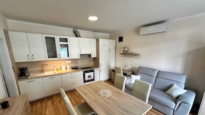 A modern kitchen with white cabinets, a wooden countertop, and a dining area with a table and chairs. - Cozy Corner Ljubljana - Modern Urban Retreat (Ljubljana)