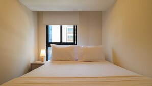 Habitación de hotel con una cama grande, una mesita de noche, una lámpara y una ventana con persianas.