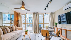 Un salon moderne comprenant un canapé, une table à manger, des chaises, un ventilateur de plafond et un téléviseur.