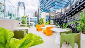 Un espace extérieur aménagé avec des tables et des chaises, entouré de verdure et avec des bâtiments modernes en arrière-plan.