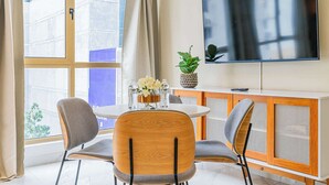 Un salon moderne avec une table de salle à manger ronde, deux chaises, un téléviseur, un meuble et une fenêtre avec des rideaux.
