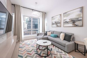 Ein modernes Wohnzimmer mit einem grauen Sofa, einem runden Couchtisch und einem großen Fernseher.