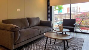 A modern living room with a sofa, a small round table, and a chair. There is a large window with a view of buildings and a balcony outside. - w Enchanting Loft w Balcony in Barranco (Lima)