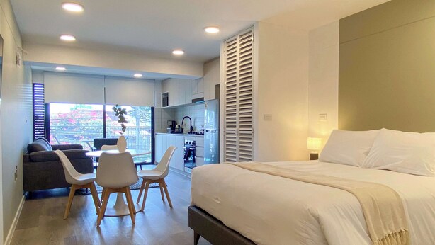 A modern hotel room with a large bed, a dining area with a table and chairs, a kitchen area, and a view of the outdoors. - w Enchanting Loft w Balcony in Barranco (Lima)