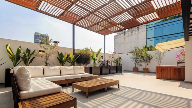 Een terras buiten met een houten bank, een bank en pottenplanten.