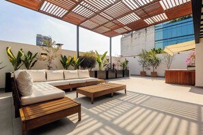 Eine Terrasse im Freien mit einer Holzbank, einer Couch und Kübelpflanzen.