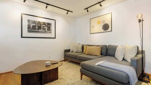 Een moderne woonkamer met een grijze bank, een ronde salontafel en een zwart-wit foto in een lijst aan de muur.