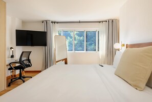 Ein Hotelzimmer mit einem großen Bett, einem Schreibtisch mit Stuhl, einem Flachbildfernseher und einem Fenster mit Vorhängen.