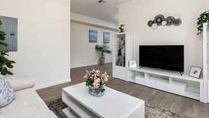 Ett modernt vardagsrum med en platt-TV, ett vitt TV-bord och en dekorativ väggdekoration.