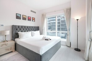 A modern hotel room with a large bed, a bedside table, a floor lamp, and a window with curtains. - A Free Housekeeping Visit FOR Every Stay Between THE 16th FEB AND THE 16th MAR - Stayshort - Stlylish 2 Bedroom in Dubai Marina That Sleeps 4 Near Met (Dubai)