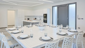 A modern dining room with a large table set for a meal, white chairs, and a kitchen in the background. - Independent Villa with Pool, Sea View, Wi-Fi, and Air Conditioning (Ugento)
