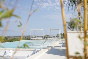 A rooftop pool with lounge chairs and a pergola, overlooking a landscape.