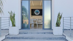 A modern building entrance with glass doors, a logo on the wall, and potted plants on either side. - Independent Villa with Pool, Sea View, Wi-Fi, and Air Conditioning (Ugento)