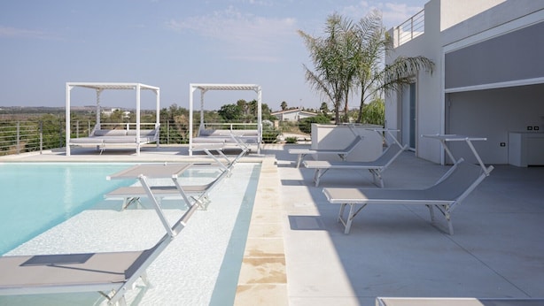 A poolside area with lounge chairs and a pergola, a building with a garage, and a clear sky. - Independent Villa with Pool, Sea View, Wi-Fi, and Air Conditioning (Ugento)
