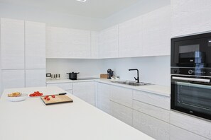 A modern kitchen with white cabinetry, a black oven, and a countertop with a cutting board and fruit.