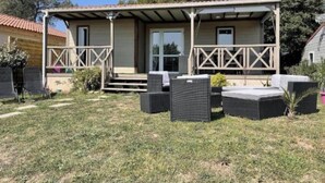 A covered outdoor seating area with a patio table and chairs, a small stage, and a door leading to a building. - Chalet Prestige - Oasis Village 5 stars - Comfort and calm (Puget-sur-Argents)