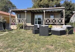 Un espace extérieur abrité, aménagé avec une table et des chaises de patio, une petite scène et une porte donnant accès à un bâtiment.