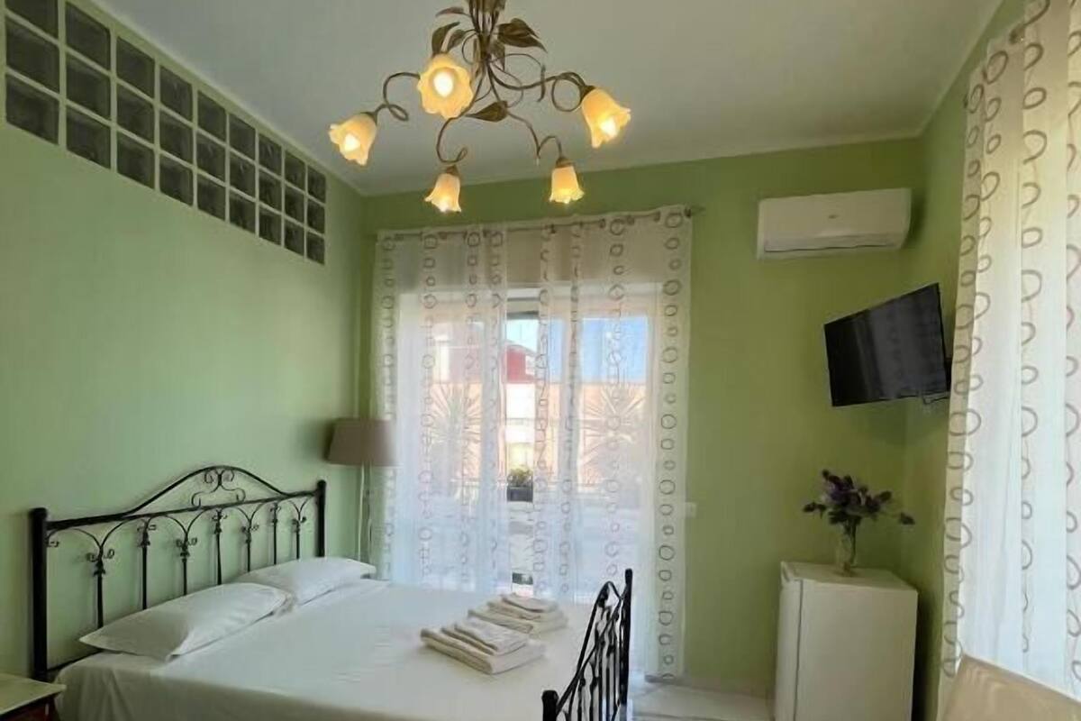 A bedroom with a bed, a chair, a TV, and a small cabinet.