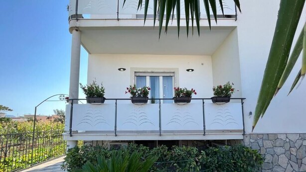 Ein zweistöckiges Gebäude mit Balkon, Pflanzkübeln und einem Kiesweg.
