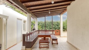 Un patio exterior con mesa y bancos de madera, una pérgola arriba y vistas al verdor.