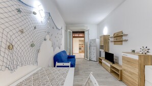 Una habitación moderna y luminosa con una mesa con diseño, una silla azul, un mueble de madera con un televisor y un adorno de red en la pared.