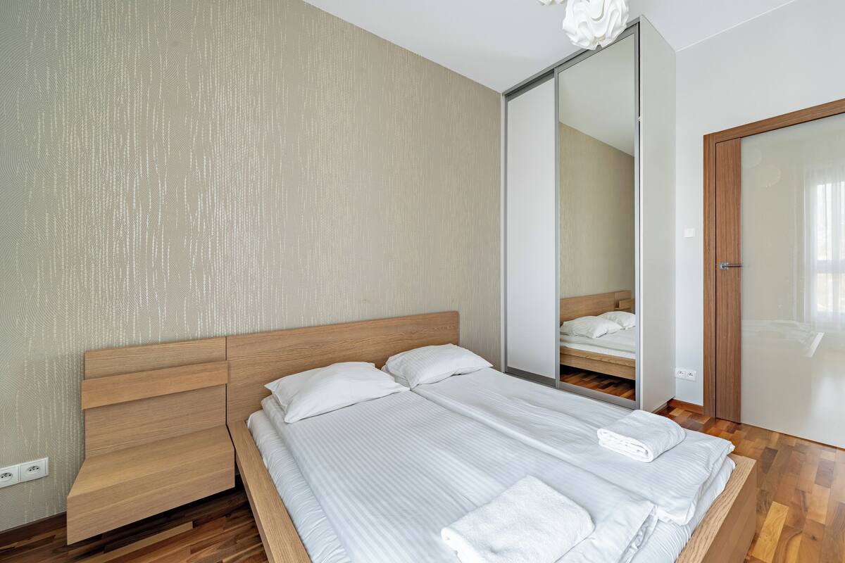 Quarto moderno com cama de madeira, um espelho grande e guarda-roupa de madeira.