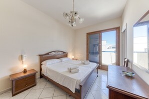 Quarto com cama, mesas de cabeceira, um candelabro, escrivaninha de madeira e porta de correr de vidro.