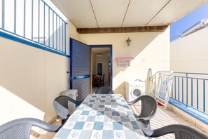 Un espace extérieur abrité, aménagé pour les repas, avec une table et des chaises, un lave-linge et une rambarde bleue.