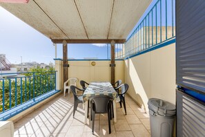 A balcony with a table and chairs, a trash bin, and a view of the city. - Apartment 'Rocco 1' with Air Conditioning (Torre San Giovanni)